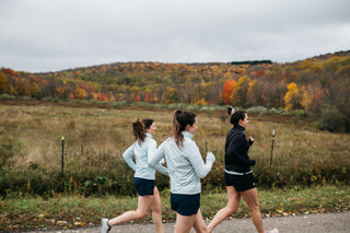 Group of three women running together down a hill in the fall.