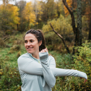 Woman stretching her arm in Middle Trail Northeast Classic quarter zip in light blue