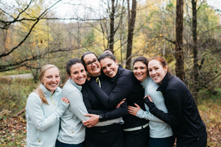 A group of 6 women all hugging each other on a Fall day wearing Middle Trail Running quarter zips to keep warm.