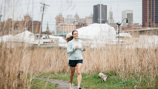 Woman running along field in Middle Trail apparel
