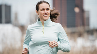 A woman smiling while running and wearing the Middle Trail Northeast Classic quarter zip in light blue