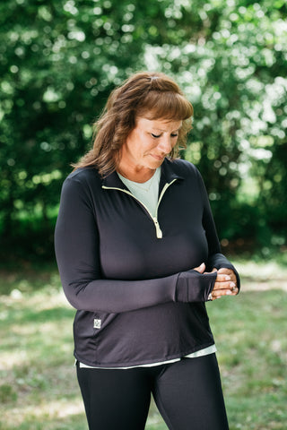 Woman wearing Middle Trail Northeast Classic quarter zip in black looking at thumb hole feature