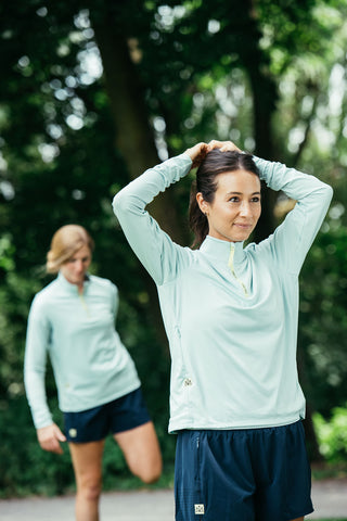 A woman in the front wearing the Middle Trail blue quarter-zip and fixing her hair as she gets ready for a run.
