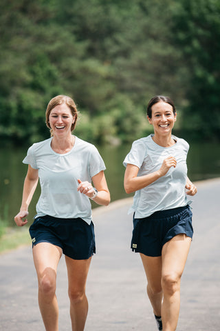 Two women runners running next to each other in the blue Middle Trail running t-shirt.