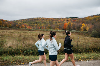 Three women runners heading down a hill in Ellicottville, NY in their Middle Trail shorts and quarter zip, enjoying the fall foliage.