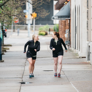 two woman wearing black quarter zips and black running shorts