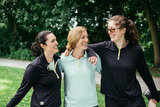 Three women runners talking and laughing in their women's running quarter zip as they stretch for a run.