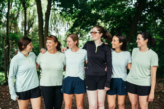 A group of six women all linking arms and laughing as they wear their Middle Trail running apparel. 
