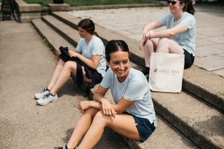 A close-up of a woman runner smiling after a run, sitting on a set of concrete stairs, with two other runners sitting behind her on the stairs relaxing after their run. 