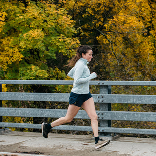 woman running in light blue quarter zip and blue running shorts in the fall