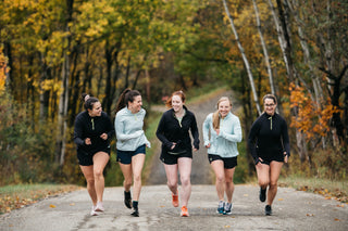 A group of five women runners laughing and running up a steep hill in Ellicottville, NY with their Middle Trail Running apparel on. 