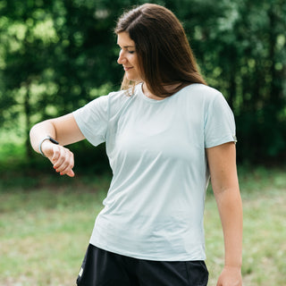 woman wearing light blue running tee and black running shorts looking at running watch