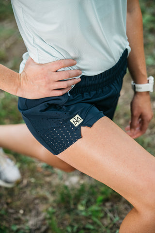 A close-up of a women's leg as she stretches to show the side ventilation of the women's running shorts.