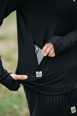 Someone tucking their phone into the built-in side pocket on the Middle Trail women's running quarter-zip. 