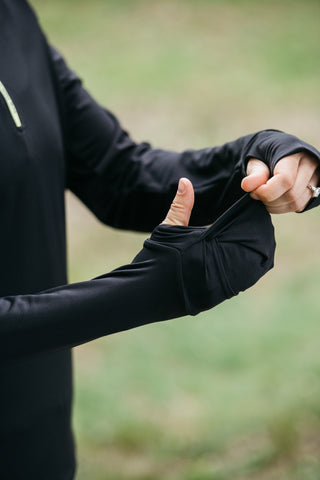 Someone showing how the built-in glove feature works and covers your hand on the black Middle Trail women's running quarter zip. 
