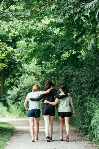Three women linking arms walking down a path away from the camera wearing Middle Trail women's running shorts.