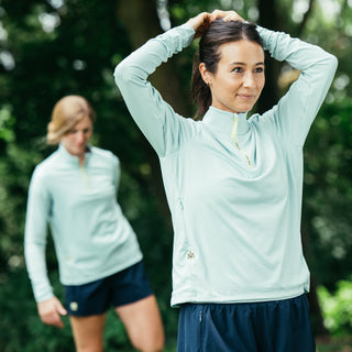 woman wearing light blue quarter zip and blue running shorts fixing ponytail