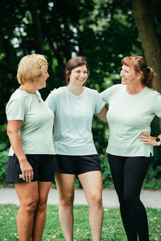 Three women linking arms, laughing, and talking in their Middle Trail t-shirts. 
