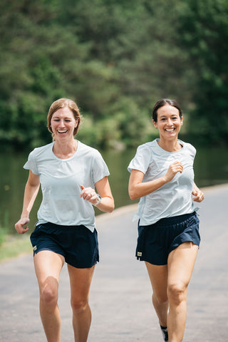 Two women runners running next to each other in the blue Middle Trail running t-shirt. 