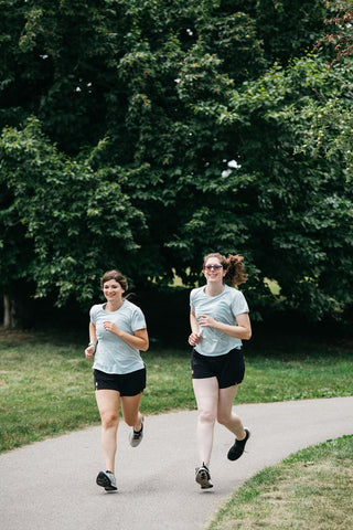 Two women running towards the camera on a path in the black Middle Trail women's running shorts.
