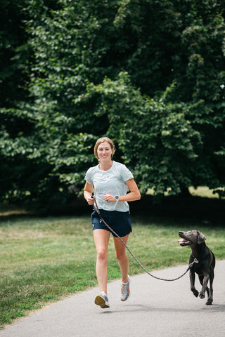 Women's Running Resources. Women running down a path with her labrador dog wearing Middle Trail running shirt and shorts.