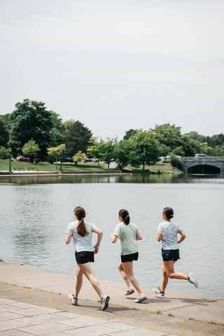 A group of three women all running together in stride down a path with one woman in the green t-shirt and the other women in the blue t-shirt.