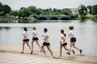 A group of five women all running together on the path around Hoyt Lake in Buffalo, NY in front of the history museum.