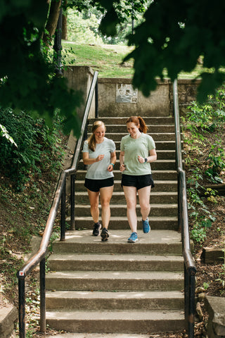 Co-Founders Genny and Kayla running together down a set of stairs laughing and enjoying the run. 