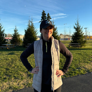 A woman smiling wearing the Middle Trail Journey Running Hat in Black with a blue MTRC icon