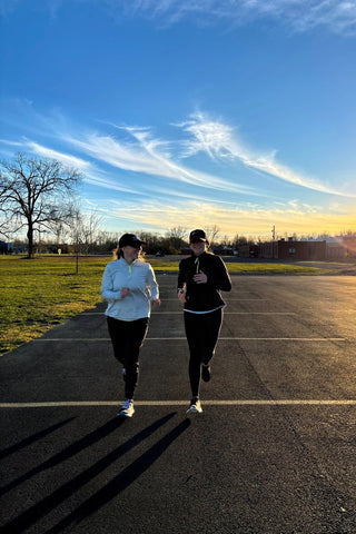 Two women running wearing the Middle Trail Northeast Classic quarter zips in light blue and black, and the Journey Running Hats